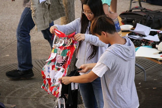 Two people hold and adjust a colorful fabric piece beside a table.